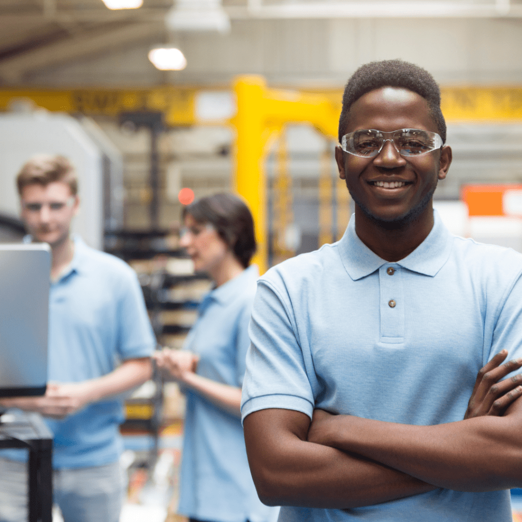 apprentice, apprenticeship, young worker, boy, blue polo shirt, goggles, arms crossed, smiling, warehouse, manufacturing, engineering, at work
